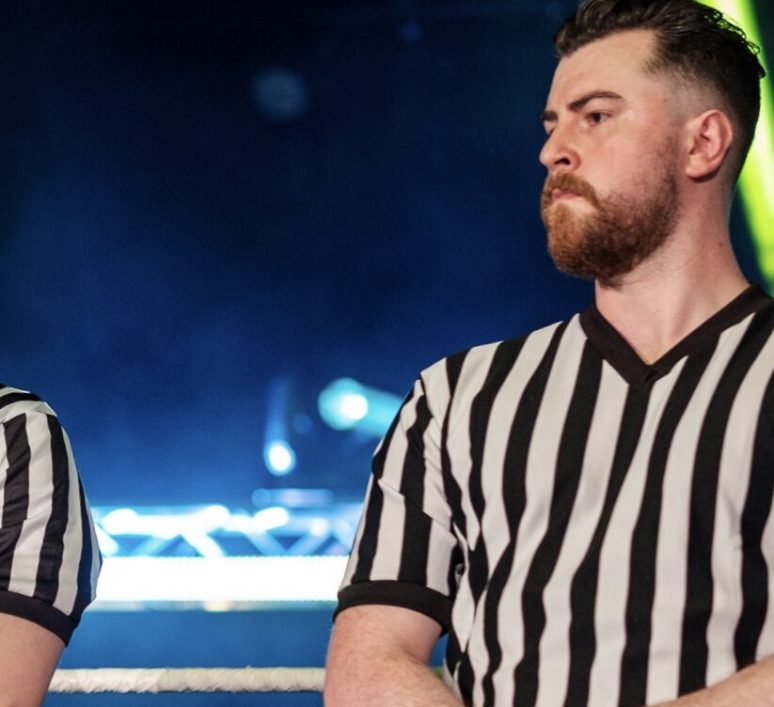 Professional wrestling referee Thomas Kearins stands in the ring with his hands folded.